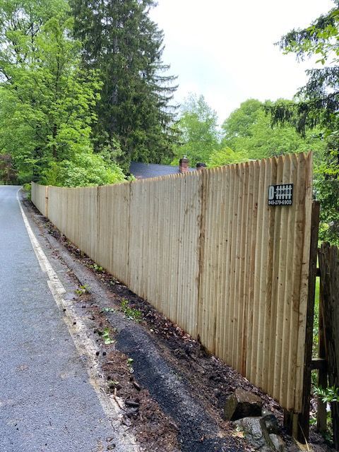 Wooden fence along a wet roadside beside trees and greenery
