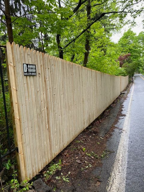 Wooden privacy fence along a wet roadside under green trees