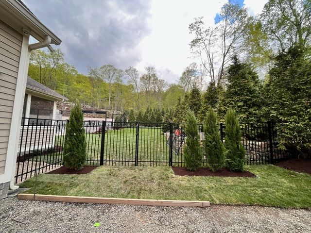 Backyard with black metal fence, trimmed shrubs, and grassy lawn beside a house