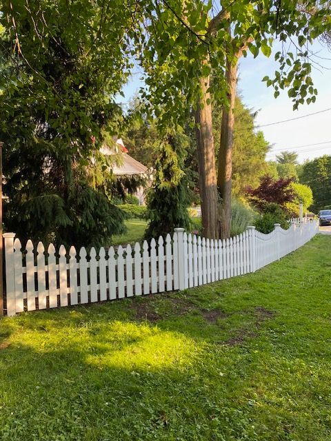 White picket fence along a sunlit green lawn beside trees and a garden path