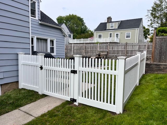 White vinyl fence and gate beside a gray house in a small backyard area