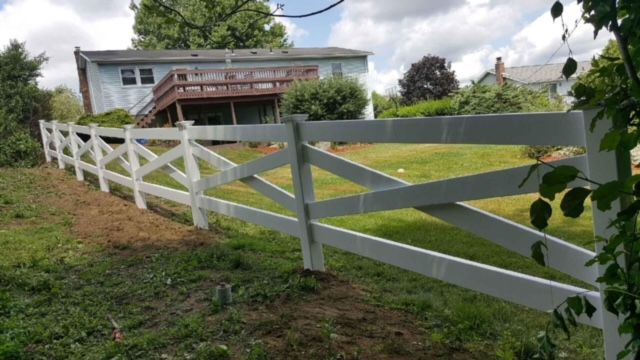 White wooden fence along a grassy hill in front of a two-story house under a cloudy sky