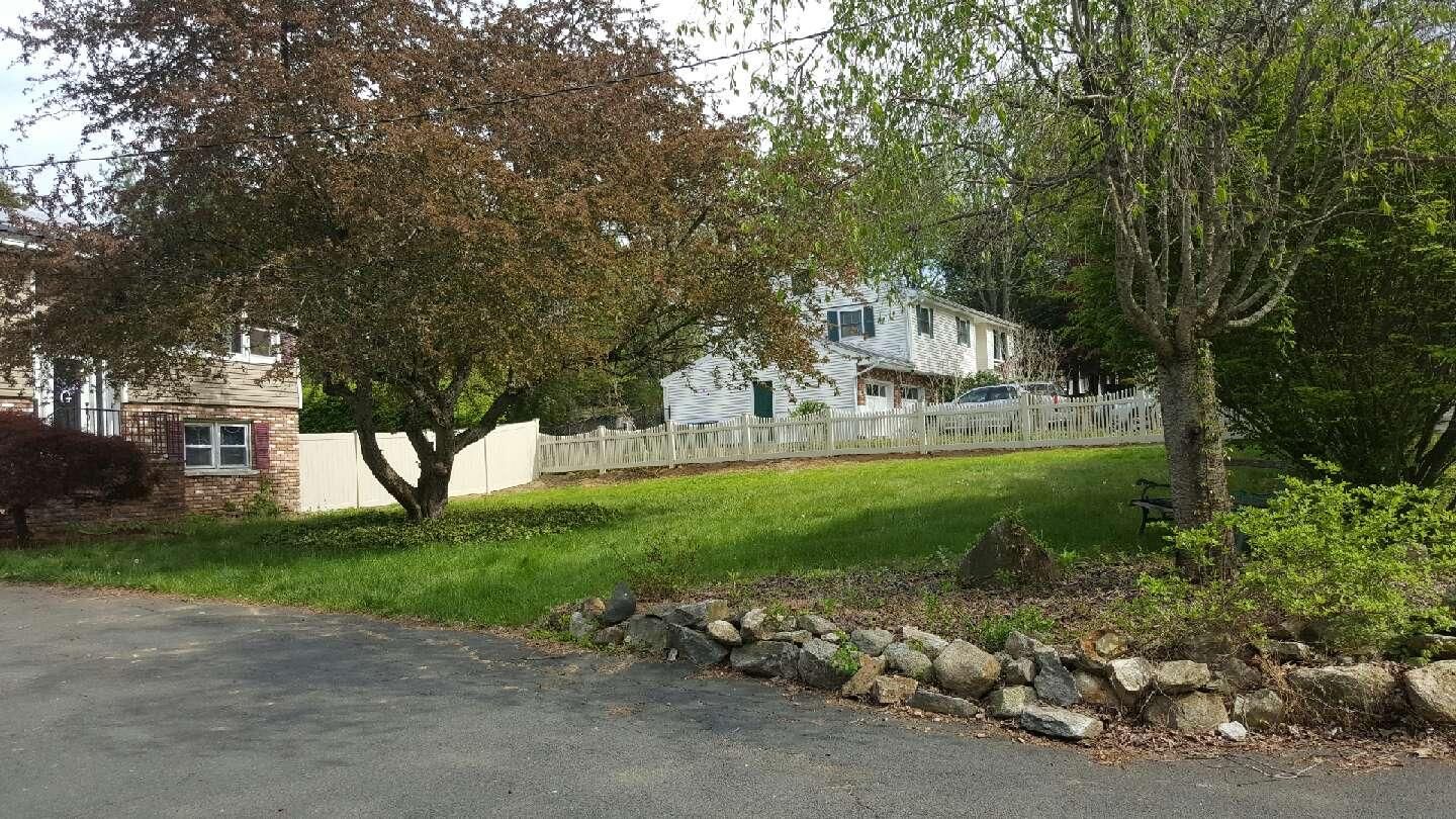 Grassy front yard with trees, a stone border, and a house in the background