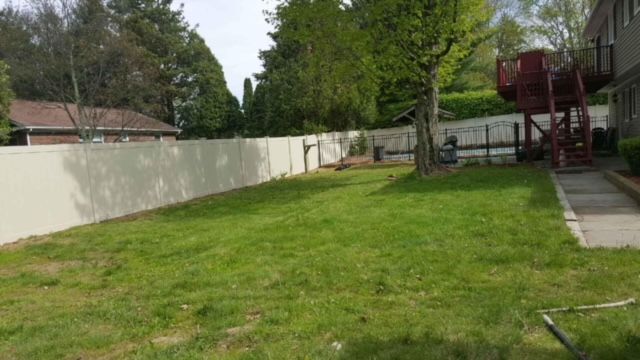 Grassy backyard with a white fence, trees, and a small patio beside a red deck.