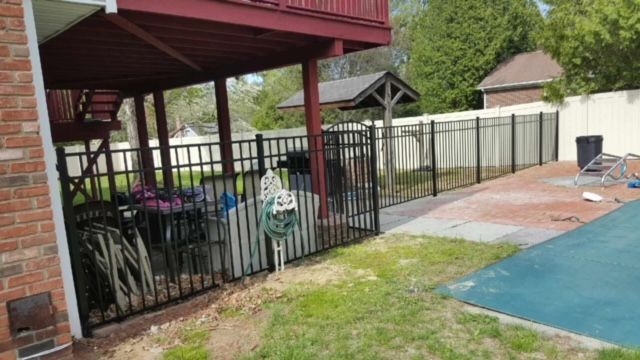 Backyard patio with black fence, bicycle, and blue pool cover beside a brick house