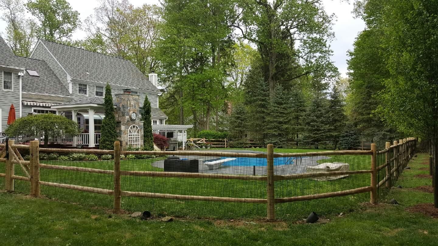 Backyard with a fenced-in blue swimming pool beside a gray house and tall green trees