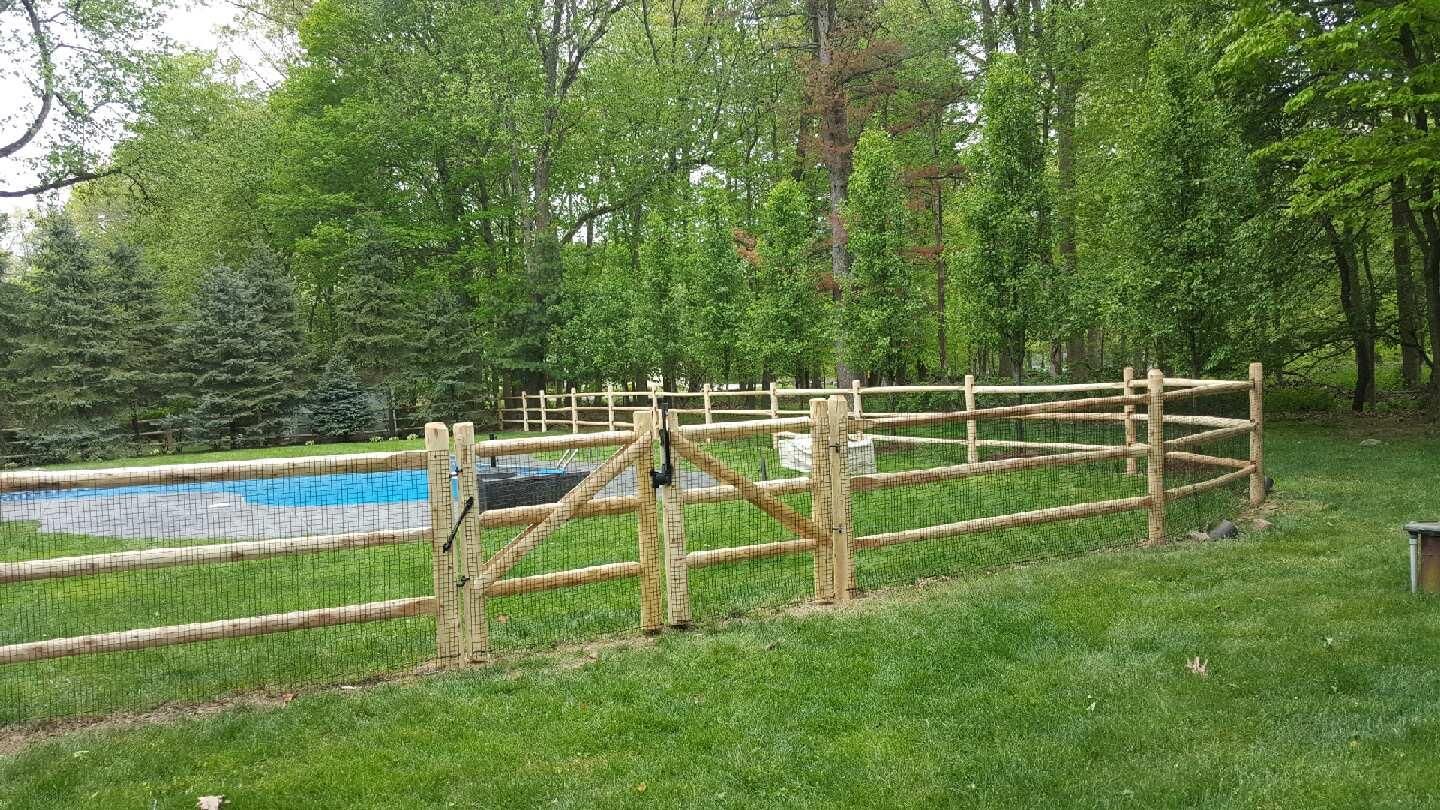 Wooden fence beside a small outdoor pool in a grassy, tree-lined yard