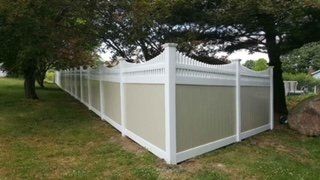 White vinyl privacy fence with tan panels enclosing a yard under large trees