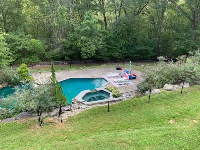 Backyard pool and hot tub beside a wooded hillside, with lounge chairs and a small patio area