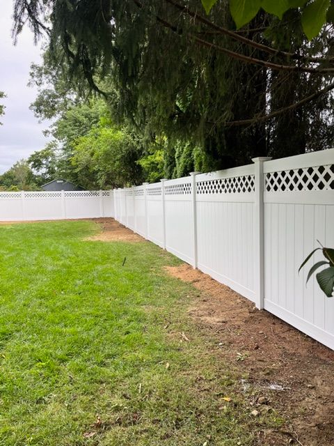 White vinyl privacy fence along a green backyard lawn with trees overhead