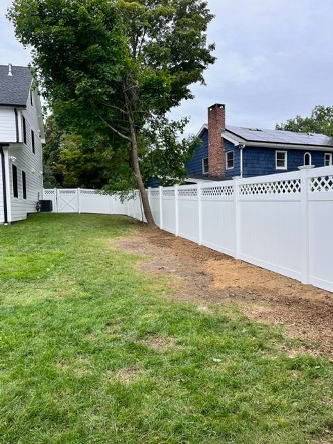 Backyard lawn beside a white fence, with a tree and neighboring houses in view