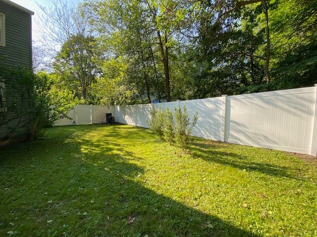 Sunny backyard with green lawn, white fence, and tall trees casting shade