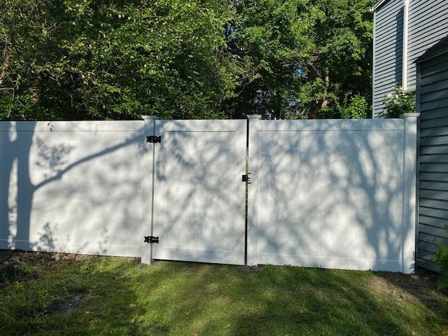 White privacy fence panels beside a green lawn, with trees casting shadows in a suburban yard.