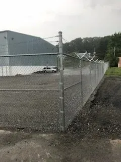 Chain-link fenced gravel lot beside a gray industrial building, with a parked white truck.
