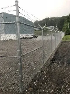 Chain-link fence around an industrial yard with gravel ground and a large white building in the background