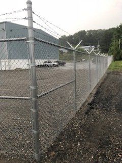 Chain-link fence around an industrial lot with barbed wire and a building in the background