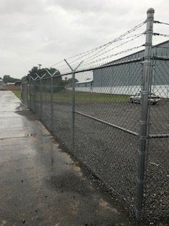 Wet chain-link fence along a paved lot under overcast skies