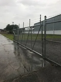 Rainy chain-link fence beside a wet sidewalk and industrial building under an overcast sky