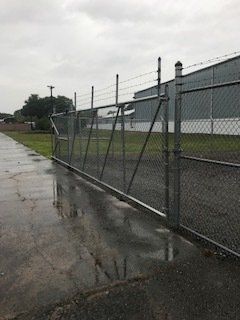 Wet chain-link fence along a rainy sidewalk beside a grassy industrial lot