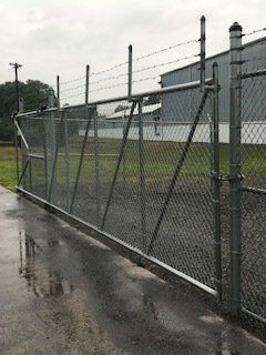 Chain-link fence beside a wet industrial road on an overcast day