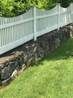 White picket fence atop a stone retaining wall beside a green lawn and trees
