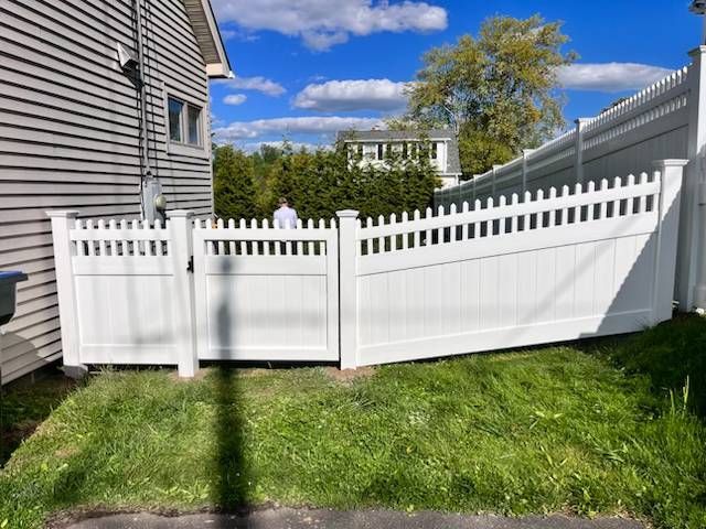 White vinyl fence and gate in a grassy backyard beside a house, under a blue sky