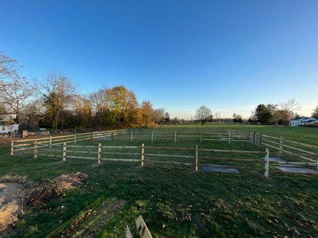 Fenced grassy field under a clear blue sky with trees in the background