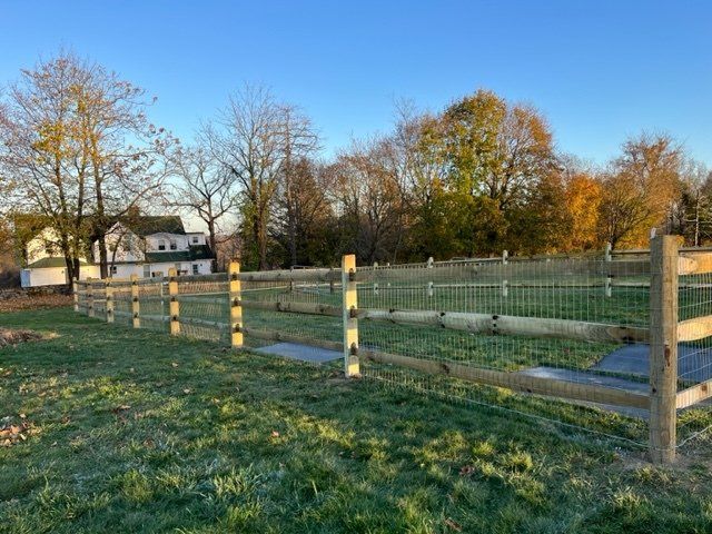 Wooden fenced grassy field at sunset with autumn trees and a house in the background