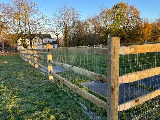Wooden fenced garden beds in a grassy yard at sunset with trees and a house in the background