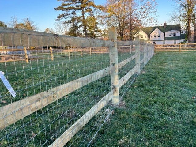 Wooden wire-mesh fence along a grassy yard with houses and trees in the background