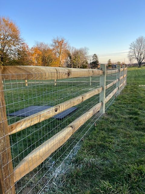 Wooden post-and-wire fence beside a grassy field under a clear blue sky at sunset