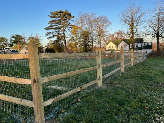 Wooden wire fence around a grassy field with trees and houses in the background at dusk