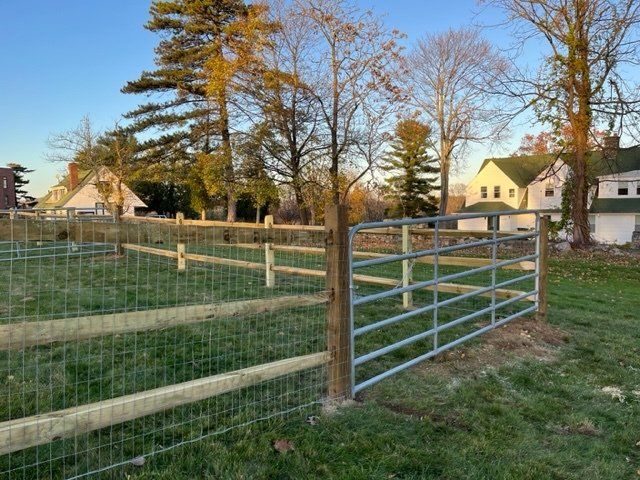 Wire fence and metal gate in a grassy yard with houses and trees in the background