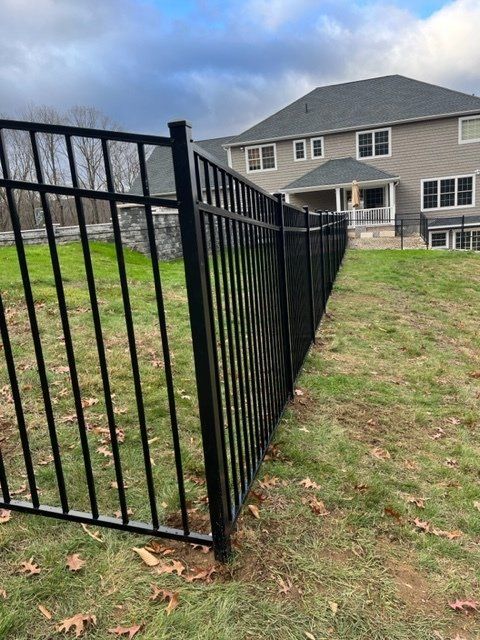 Black metal fence along a grassy yard beside a gray house under a cloudy sky.