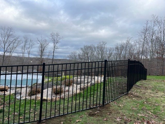 Black metal fence beside a pool and rocky shoreline under a cloudy sky