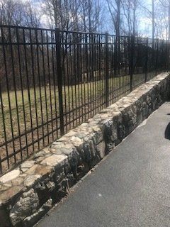 Stone retaining wall beside a black metal fence along a paved path in a leafless park