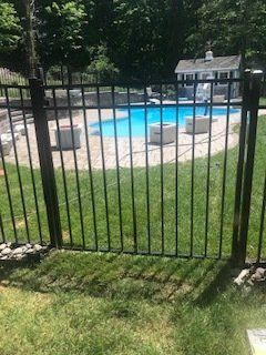 Black metal fence overlooking a backyard pool with patio chairs and green lawn.