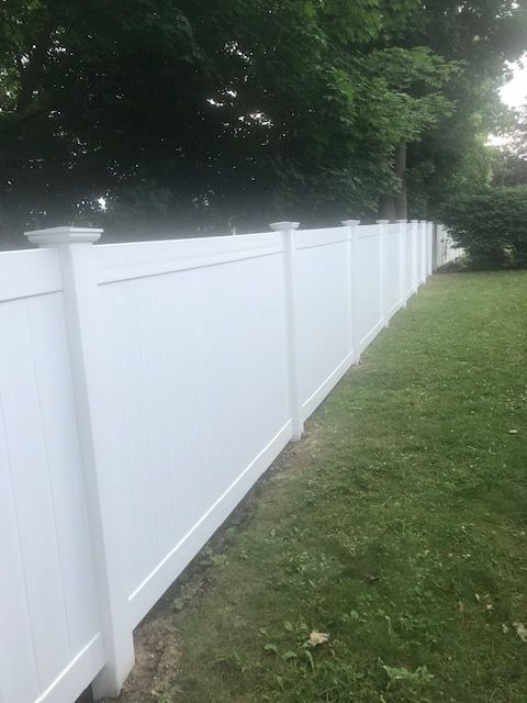 White vinyl fence along a grassy yard with trees in the background