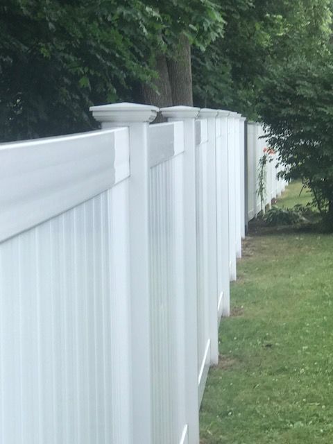 White vinyl fence along a grassy yard with trees in the background