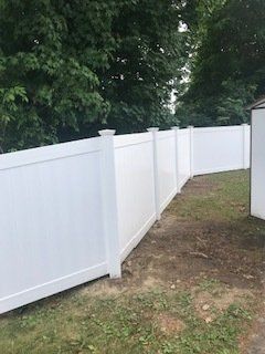 White vinyl fence along a grassy yard beside trees and a house exterior
