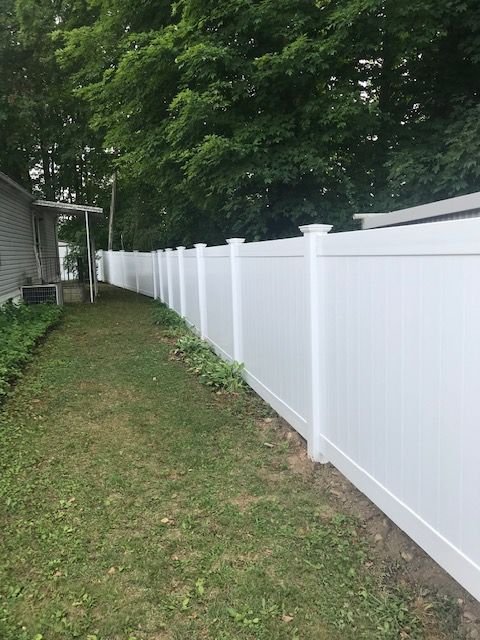 Long white vinyl fence along a grassy side yard beside a house and trees