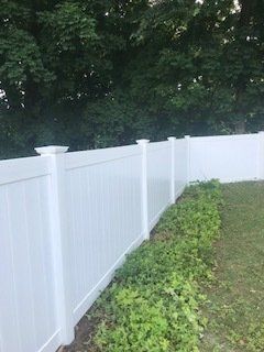 White vinyl fence curving along a grassy yard beside dense green trees