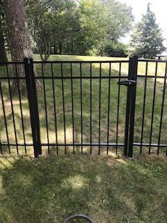 Black metal gate in a grassy yard with trees in the background.