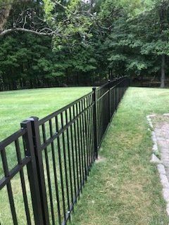Black metal fence along a grassy yard beside trees and a stone path