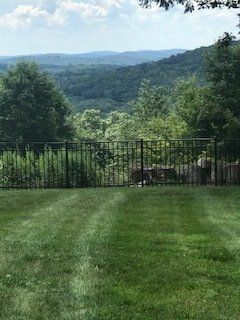 Lush green lawn with a black fence overlooking forested hills and distant mountains under a clear sky