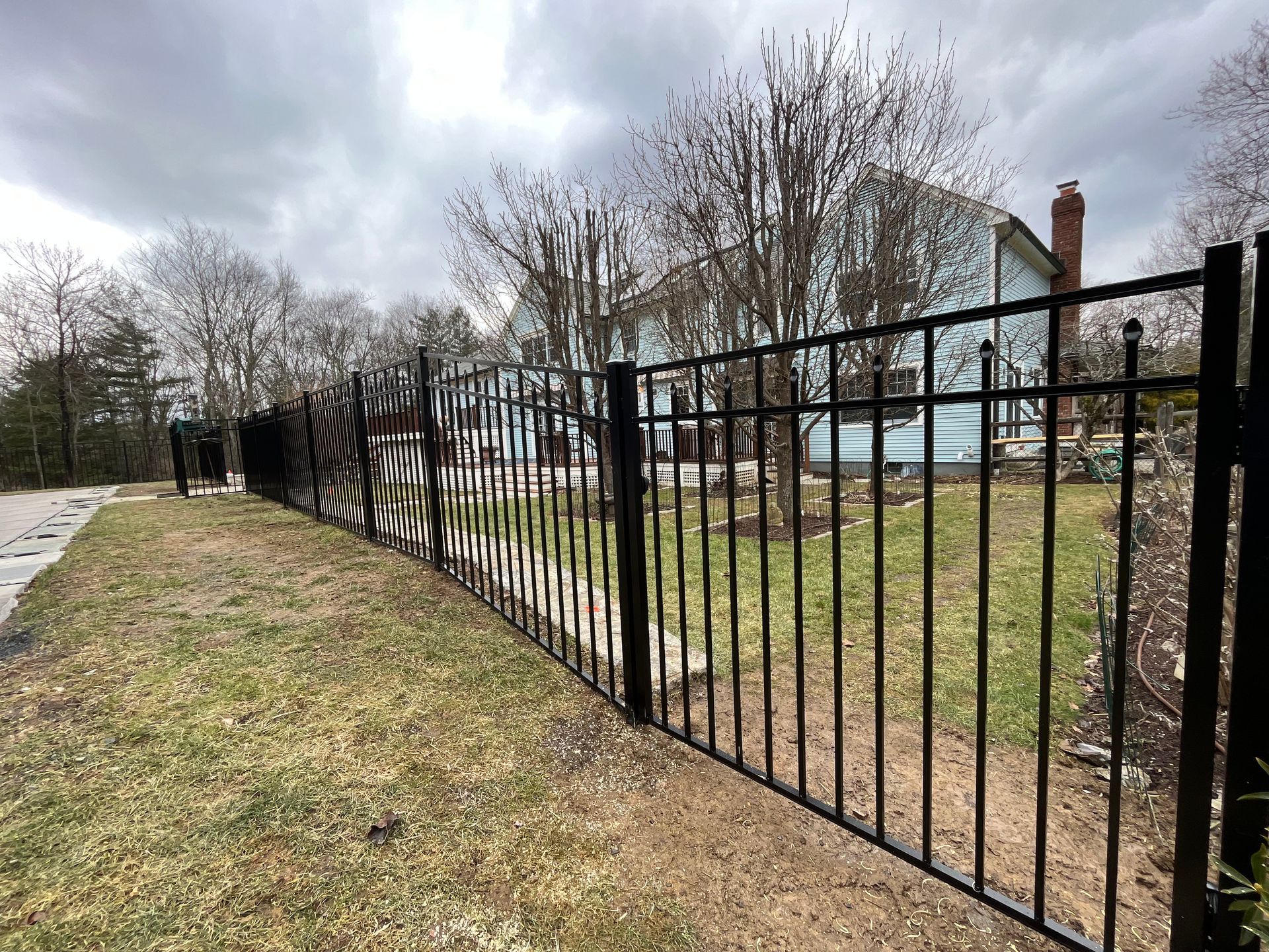 Black metal fence along a grassy path beside houses under a cloudy sky
