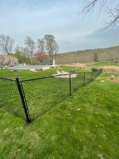 Backyard with black chain-link fence, green lawn, and a small pool beside trees and hills