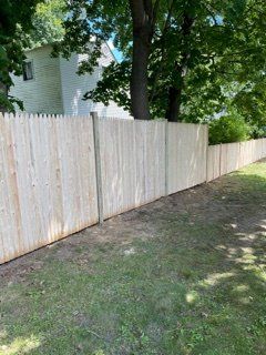 White wooden fence along a grassy yard beside a tree and house.