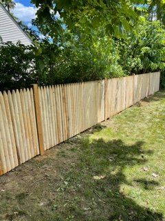 Wooden privacy fence along a grassy yard beside a house under leafy trees.