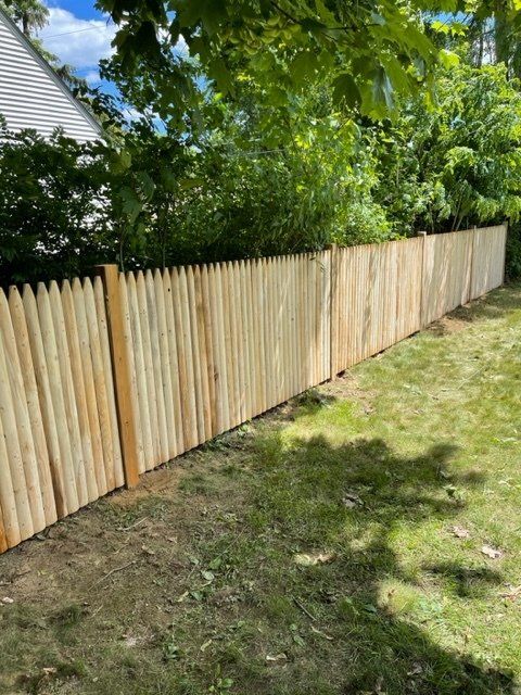 Wooden privacy fence along a grassy yard under leafy green trees in sunlight